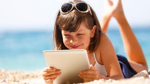Ein Mädchen liegt am Strand und schaut auf ihr Tablet