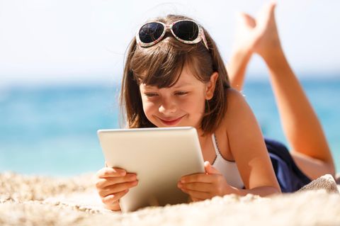 Ein Mädchen liegt am Strand und schaut auf ihr Tablet