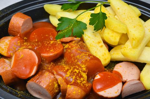 Eine in Stücke geschnittene Wurst liegt in einer Currysauce. Daneben Pommes und ein wenig glatte Petersilie