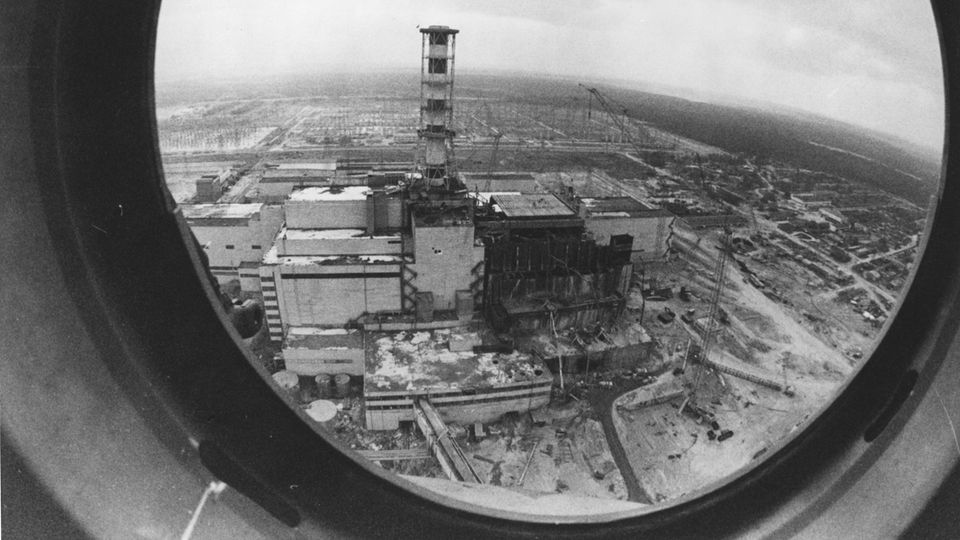 Ein Schwarz-weiß-Foto zeigt den explodierten Reaktor von Tschernobyl durch ein rundes Hubschrauber-Fenster