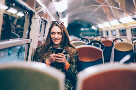 Frau sitzt in Bahn mit Handy in der Hand