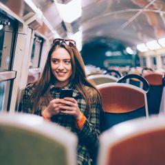 Frau sitzt in Bahn mit Handy in der Hand