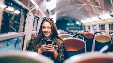 Frau sitzt in Bahn mit Handy in der Hand