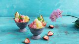 Shave Ice  Für das Shave Ice: 600 ml frisches Trinkwasser  Für den Ananassirup: 1 Ananas (ca. 800 g), 100 g Zucker  Für den Erdbeersirup: 250 g Erdbeeren, 100 g Zucker  Für den Vanillesirup: 1 Vanilleschote, 100 g Zucker  Außerdem: Eiswürfelformen, 3 Flaschen (à 250 ml), Standmixer (am besten mit Ice-Crush-Funktion), alternativ gekaufter Sirup (z. B. von Monin)      Zubereitung:  Am Vortag für das Shave Ice das Wasser in 2–3 Eiswürfelformen füllen und mindestens 10 Stunden einfrieren.      Für den Ananassirup die Ananas schälen, vierteln, den Strunk herausschneiden und das Fruchfleisch in 3 cm große Würfel schneiden. 2 schöne Würfel als Garnitur beiseitelegen. Die Ananas mit 250 ml Wasser in einen hohen Mixbecher geben und mit dem Pürierstab fein pürieren. Das Fruchtpüree durch ein feines Sieb in einen Topf gießen. Den Ananassaft mit dem Zucker verrühren und bei mittlerer Hitze zum Kochen bringen. Dabei aufsteigenden Schaum mit einer Kelle abschöpfen. Den Ananassirup 15 Minuten kochen lassen, dann in eine sterile Flasche umfüllen und verschließen.      Für den Erdbeersirup die Erdbeeren waschen, den Kelch entfernen und die Erdbeeren klein würfeln. 1 EL als Garnitur beiseitelegen. Die Erdbeeren mit 250 ml Wasser in einen Topf geben und bei mittlerer Hitze zum Kochen bringen. Sich bildenden Schaum abschöpfen. Die Erdbeeren so lange kochen, bis die rote Farbe in das Wasser übergegangen ist. Die Flüssigkeit durch ein feines Sieb in einen weiteren Topf gießen. Die Erdbeeren nicht durchpressen, da der Sirup sonst trüb wird. Den Zucker in den Erdbeersaft geben, zum Kochen bringen und so lange kochen, bis er sich aufgelöst hat. Den Sirup in eine sterile Flasche umfüllen und verschließen.      Für den Vanillesirup die Schote längs aufschneiden und das Mark mit dem Messer herauskratzen. Vanillemark und Schote mit 300 ml Wasser und dem Zucker in einen Topf geben und zum Kochen bringen. 15 Minuten bei mittlerer Hitze kochen lassen. Die Vanilleschote entfernen und den Sirup in eine sterile Flasche umfüllen und verschließen.      Am nächsten Tag die Eiswürfel portionsweise in einen Mixer geben und zu feinem Schnee hacken. Dafür die Eiswürfel gegebenenfalls vorher in einen Gefrierbeutel geben und mit einem Fleischklopfer oder Nudelholz etwas zerkleinern, dann erst in den Mixer geben. Das gehackte Eis in ein Eisschälchen geben und mit der Hand zu einer Kuppel formen. Je ein Drittel der Kuppel mit dem jeweiligen Sirup (alternativ gekaufter Sirup) tränken. Shave Ice mit Ananas und Erdbeeren garnieren und servieren. Nicht wieder einfrieren, da es sonst zu einem Eisblock gefriert.