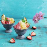 Shave Ice  Für das Shave Ice: 600 ml frisches Trinkwasser  Für den Ananassirup: 1 Ananas (ca. 800 g), 100 g Zucker  Für den Erdbeersirup: 250 g Erdbeeren, 100 g Zucker  Für den Vanillesirup: 1 Vanilleschote, 100 g Zucker  Außerdem: Eiswürfelformen, 3 Flaschen (à 250 ml), Standmixer (am besten mit Ice-Crush-Funktion), alternativ gekaufter Sirup (z. B. von Monin)      Zubereitung:  Am Vortag für das Shave Ice das Wasser in 2–3 Eiswürfelformen füllen und mindestens 10 Stunden einfrieren.      Für den Ananassirup die Ananas schälen, vierteln, den Strunk herausschneiden und das Fruchfleisch in 3 cm große Würfel schneiden. 2 schöne Würfel als Garnitur beiseitelegen. Die Ananas mit 250 ml Wasser in einen hohen Mixbecher geben und mit dem Pürierstab fein pürieren. Das Fruchtpüree durch ein feines Sieb in einen Topf gießen. Den Ananassaft mit dem Zucker verrühren und bei mittlerer Hitze zum Kochen bringen. Dabei aufsteigenden Schaum mit einer Kelle abschöpfen. Den Ananassirup 15 Minuten kochen lassen, dann in eine sterile Flasche umfüllen und verschließen.      Für den Erdbeersirup die Erdbeeren waschen, den Kelch entfernen und die Erdbeeren klein würfeln. 1 EL als Garnitur beiseitelegen. Die Erdbeeren mit 250 ml Wasser in einen Topf geben und bei mittlerer Hitze zum Kochen bringen. Sich bildenden Schaum abschöpfen. Die Erdbeeren so lange kochen, bis die rote Farbe in das Wasser übergegangen ist. Die Flüssigkeit durch ein feines Sieb in einen weiteren Topf gießen. Die Erdbeeren nicht durchpressen, da der Sirup sonst trüb wird. Den Zucker in den Erdbeersaft geben, zum Kochen bringen und so lange kochen, bis er sich aufgelöst hat. Den Sirup in eine sterile Flasche umfüllen und verschließen.      Für den Vanillesirup die Schote längs aufschneiden und das Mark mit dem Messer herauskratzen. Vanillemark und Schote mit 300 ml Wasser und dem Zucker in einen Topf geben und zum Kochen bringen. 15 Minuten bei mittlerer Hitze kochen lassen. Die Vanilleschote entfernen und den Sirup in eine sterile Flasche umfüllen und verschließen.      Am nächsten Tag die Eiswürfel portionsweise in einen Mixer geben und zu feinem Schnee hacken. Dafür die Eiswürfel gegebenenfalls vorher in einen Gefrierbeutel geben und mit einem Fleischklopfer oder Nudelholz etwas zerkleinern, dann erst in den Mixer geben. Das gehackte Eis in ein Eisschälchen geben und mit der Hand zu einer Kuppel formen. Je ein Drittel der Kuppel mit dem jeweiligen Sirup (alternativ gekaufter Sirup) tränken. Shave Ice mit Ananas und Erdbeeren garnieren und servieren. Nicht wieder einfrieren, da es sonst zu einem Eisblock gefriert.