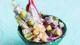 Acai-Bowl mit Kiwi-Pitaya-Spiessen  Für die Bowl: 1 Banane, 200 g TK-Erdbeeren, 100 g griechischer Joghurt, 100 ml Kokosnussmilch, 2 EL Açaípulver   Für das Granola: 2 EL kandierte Ananas, 2 EL geröstete, gesalzene Erdnusskerne, 4 EL Haferflocken, 4 EL Kokoschips, 2 EL Kokosöl, 3 EL Honig, 1 EL Rohrohrzucker, Salz, 2 EL Kokosraspel  Für das Topping: 4 Holzspieße (à 10 cm), 1 Pitaya (Drachenfrucht), 2 Kiwis, 1 EL Kokosöl, 1 EL Honig      Zubereitung:  Für die Bowl die Banane schälen, in 0,5 cm dicke Scheiben schneiden und mindestens 2 Stunden, oder über Nacht, einfrieren.      Für das Granola den Backofen auf 175 °C Ober-/Unterhitze vorheizen. Ein Backblech mit Backpapier auslegen. Die Ananas möglichst klein schneiden, besser mithilfe einer Küchenmaschine fein hacken. Die Erdnusskerne mit dem Messer grob hacken. Ananas, Erdnüsse, Haferflocken und Kokoschips in einer Schale mischen. Kokosöl, Honig, Zucker und 1 Prise Salz mischen. Dafür entweder in der Mikrowelle in einer geeigneten Schale für einige Sekunden erwärmen oder in einer hitzebeständigen Schale kurz im aufheizenden Ofen verflüssigen.      Die Honigmischung über die Kokosmischung träufeln und alles miteinander vermischen, bis die Kokosmischung gleichmäßig damit überzogen ist. Auf das Backblech geben und zu einem Quadrat von etwa 20 3 20 cm verteilen. Das Blech in den heißen Ofen (Mitte) schieben und das Granola 5 Minuten backen. Herausnehmen, die Kokosraspel über das Granola streuen, unterheben und weitere 5 Minuten backen. Das Blech aus dem Ofen nehmen und vollständig abkühlen lassen. Das ausgekühlte Granola mit den Händen zerbröseln und beiseitestellen.      Für das Topping die Spieße für 15 Minuten in Wasser legen. Inzwischen die Drachenfrucht halbieren, das Fruchtfleisch mit einem Löffel vorsichtig herausheben. Die Kiwis schälen. Beide Früchte in ca. 2 cm große Würfel schneiden. Die Fruchtwürfel abwechselnd auf die Spieße stecken. Den Rest beiseitelegen. Das Öl in einer Grillpfanne erhitzen. Die Spieße bei mittlerer Hitze von jeder Seite kurz anbraten. Anschließend mit Honig beträufeln und noch einmal in der Pfanne wenden, damit sie ringsum überzogen sind.      Gefrorene Banane, Erdbeeren, Joghurt, Kokosnussmilch und Açaípulver in einen Mixer geben. Den Mixer auf kleinster Stufe starten, dann alles auf höchster Stufe so lange pürieren, bis ein cremiges Fruchtmus entstanden ist. Das Açaímus auf zwei Schalen verteilen, zur Hälfte mit Granola und zur Hälfte mit den restlichen Fruchtwürfeln bestreuen. Als Deko je 2 Spieße darauflegen und servieren.