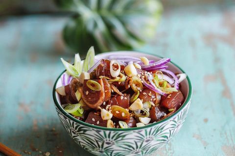 Ahi Poke - Thunfischsalat  300 g Thunfisch (Sashimiqualität), 1 kleine rote Zwiebel, 2 Frühlingszwiebeln, 1 EL Macadamianusskerne, 2 TL Sesam, 2 EL Sojasoße, 1 EL Sesamöl, 1 EL Sriracha (Chilisoße), 1 TL Honig, Salz      Zubereitung:  Den Thunfisch waschen und trocken tupfen, anschließend in mundgerechte Würfel von ca. 2 3 2 cm schneiden. Die Zwiebel schälen, halbieren und in dünne Streifen schneiden. Die Frühlingszwiebeln putzen, waschen und in feine Ringe schneiden. Die Nüsse grob hacken. Eine kleine Pfanne ohne Fett erhitzen. Nüsse und Sesam in der heißen Pfanne knapp 1 Minute goldbraun rösten, bis sie zu duften beginnen. Dann gleich aus der Pfanne nehmen, damit sie durch die Resthitze nicht verbrennen, und abkühlen lassen.      Den Fisch mit je der Hälfte der Zwiebeln, der Nüsse und des Sesams in eine Schüssel geben. Sojasoße, Öl, Sriracha und Honig dazugeben und alles miteinander vermischen. Der Fisch soll von einer glänzenden Schicht aus Marinade überzogen sein. Nach Belieben mit etwas Salz abschmecken und in zwei Schalen abfüllen. Mit restlichen Zwiebeln, Nüssen und Sesam bestreuen und servieren.
