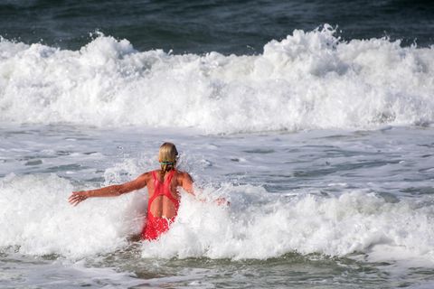Eine blonde Frau im roten Badeanzug springt in die Wellen der Nordsee vor Sylt
