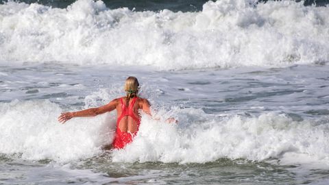 Eine blonde Frau im roten Badeanzug springt in die Wellen der Nordsee vor Sylt