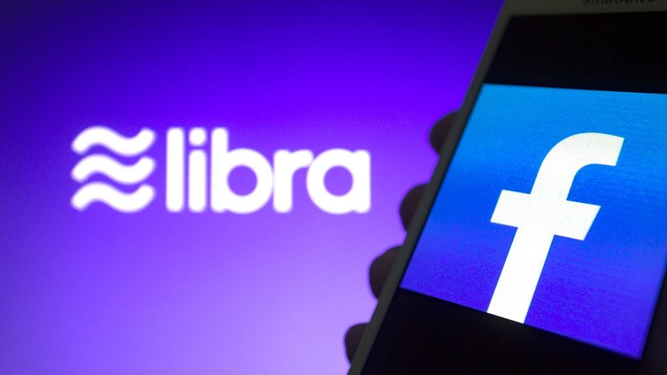 Das Libra-Logo ist vor einem Smartphone mit Facebook-Logo zu sehen