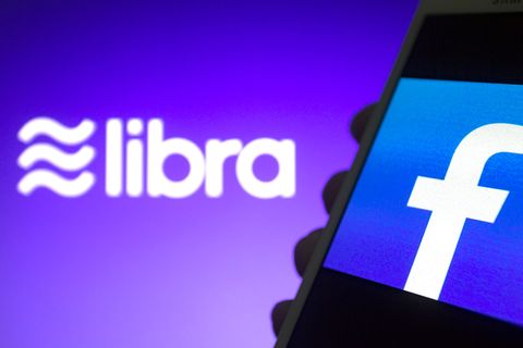 Das Libra-Logo ist vor einem Smartphone mit Facebook-Logo zu sehen