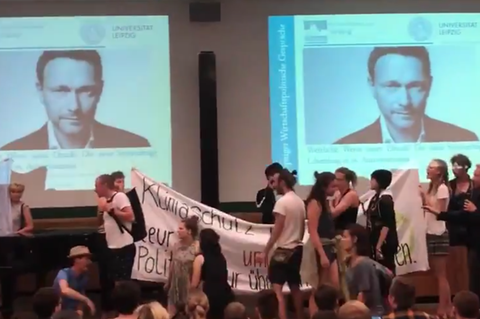 Auf einer Bühne stehen junge Menschen mit Bannern, im Hintergrund sind zwei Porträts von Christian Lindner projeziert