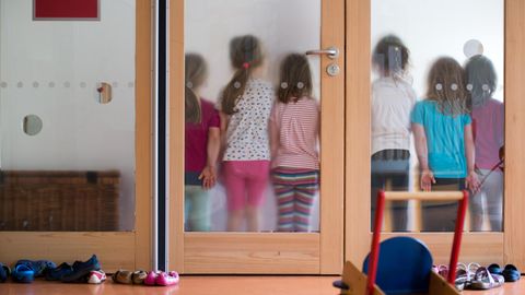 Kinder stehen in Kita hinter einer Glasscheibe