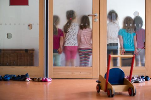 Kinder stehen in Kita hinter einer Glasscheibe