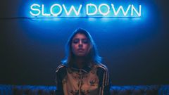Neon-Schrift "Slow Down" und Frau mit ernstem Gesicht.