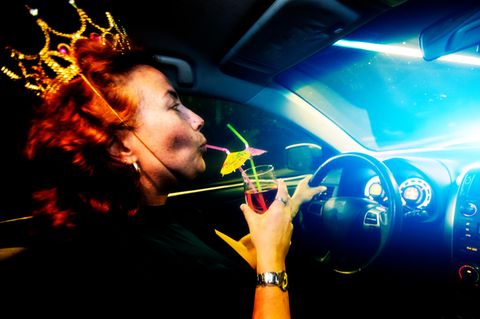 Eine Frau sitzt am Steuer eines Autos und trinkt Alkohol