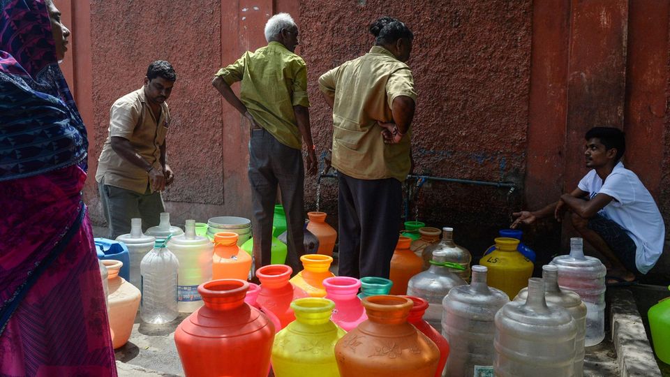 Indische Männer stehen an einer Ausgabestelle an, um Wasser in mitgebrachte Behälter abzufüllen. Indische Männer stehen an einer Ausgabestelle an, um Wasser in mitgebrachte Behälter abzufüllen.