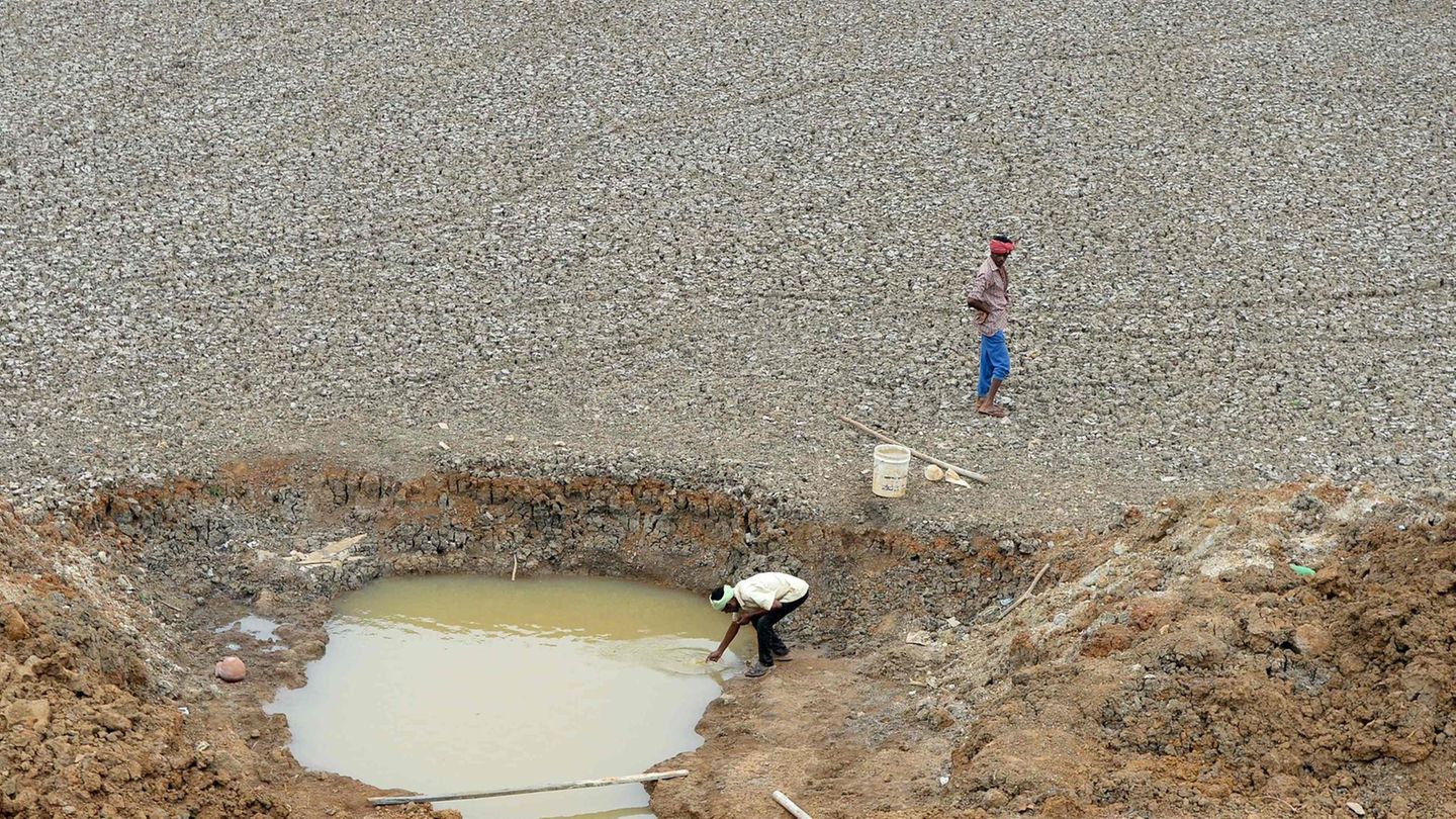 Zwei Männer stehen an einem Wasserloch, um Trinkwasser abzufüllen.