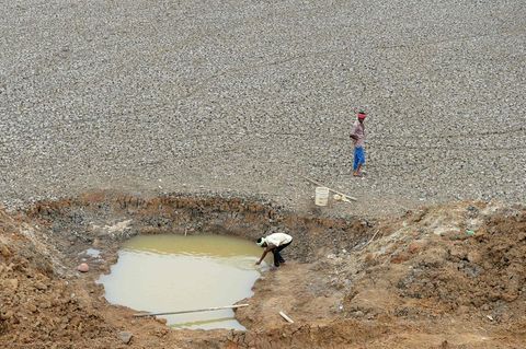 Zwei Männer stehen an einem Wasserloch, um Trinkwasser abzufüllen.