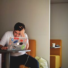 Junger Mann sitzt verzweifelt vor dem Computer.