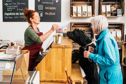Verkäuferin reicht Hund einen Snack über Thresen