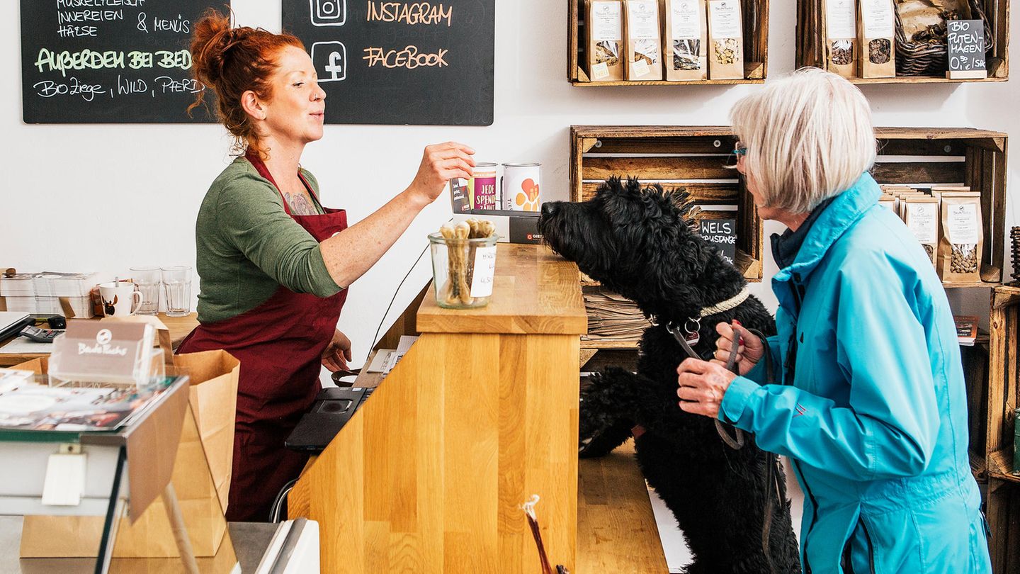 Verkäuferin reicht Hund einen Snack über Thresen