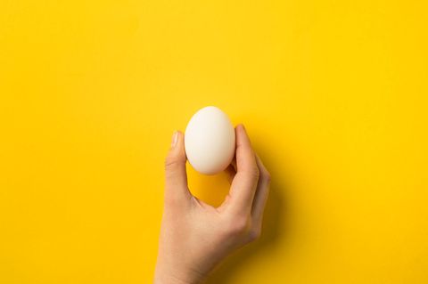Eine Hand mit Ei auf einem gelben Hintergrund