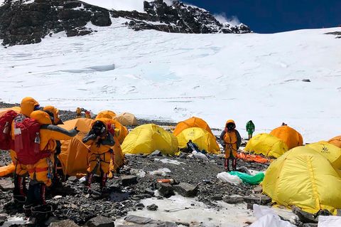 Bergsteiger in dicken Jacken stehen im Basiscamp am Mount Everest zwischen lauter verlassenen Zelten.Im Hintergrund liegt Schnee