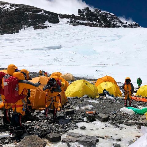 Bergsteiger in dicken Jacken stehen im Basiscamp am Mount Everest zwischen lauter verlassenen Zelten.Im Hintergrund liegt Schnee
