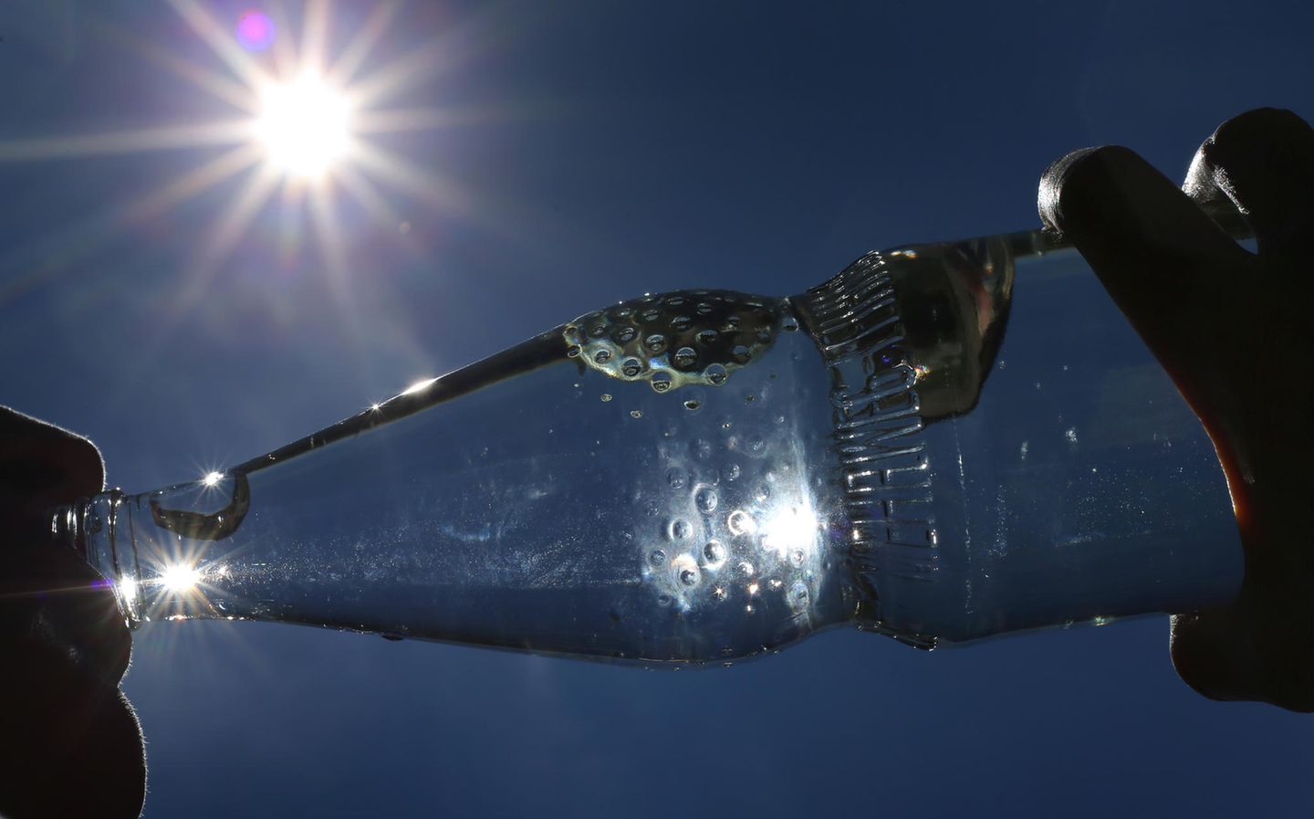 Hitzewelle – Frau trinkt bei Sonnenschein aus einer Wasserflasche