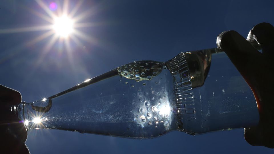 Hitzewelle – Frau trinkt bei Sonnenschein aus einer Wasserflasche