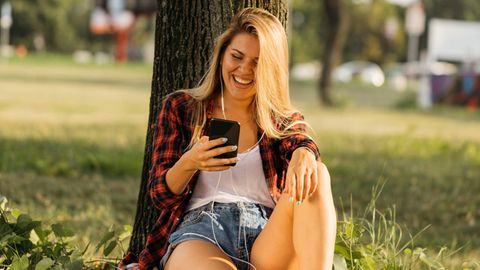 Eine Frau sitzt im Sommer mit dem Smartphone im Park