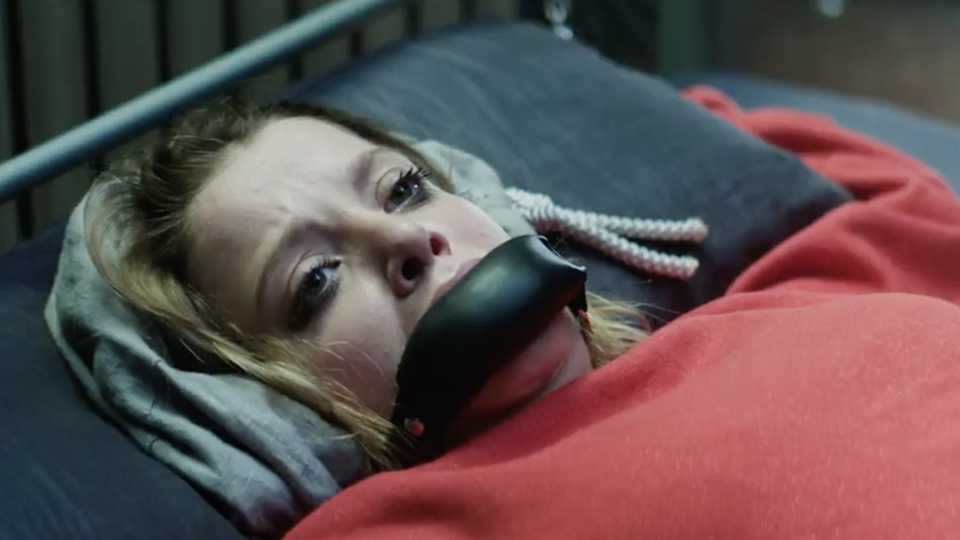 Jella Haase in "Kidnapping Stella" auf Netflix Eine junge blonde Frau liegt mit schwarzem Leder-Knebel auf einem Metallbett, an dessen Kopfende ihre Hände gefesselt sind