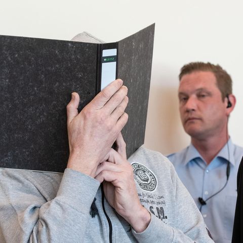 Hauptangeklagter im Fall Lügde mit Aktenordner vor dem Gesicht - im Hintergrund ein Wachmann