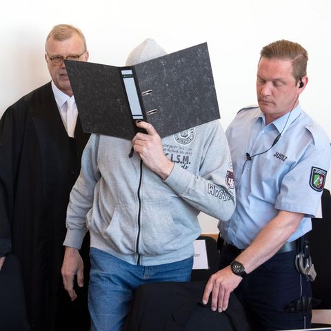Der Angeklagte Andreas V. betritt mit einem Aktenordner vor dem Gesicht den Gerichtssaal