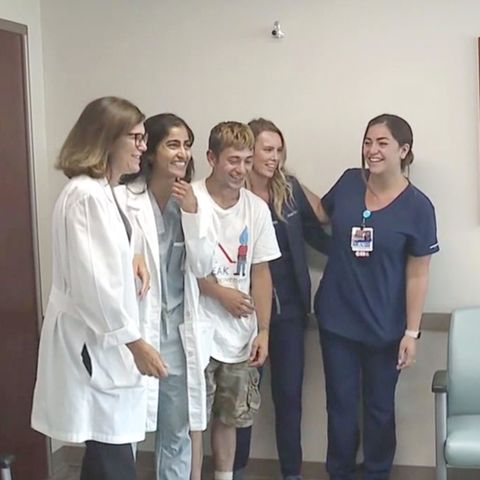 Eine Gruppe junger Menschen steht lachend in einem Krankenhaus, als wollten sie ein Gruppenfoto machen.