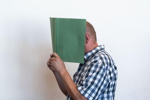 Heiko V. verdeckt sein Gesicht mit einer Aktenmappe.