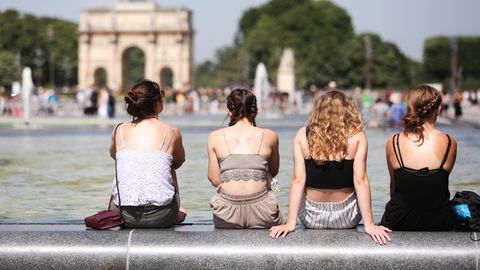 Vier Frauen sitzen bei heißen Temperaturen am Louvre auf dem Beckenrand eines Springbrunnens