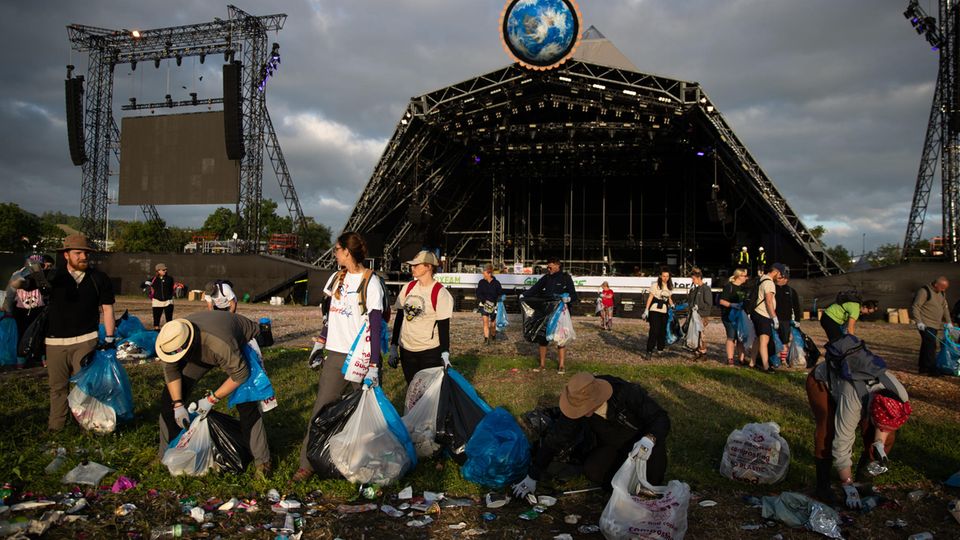 Mit Müllbeuteln ausgestattet, räumen Helfer das Festivalgelände auf