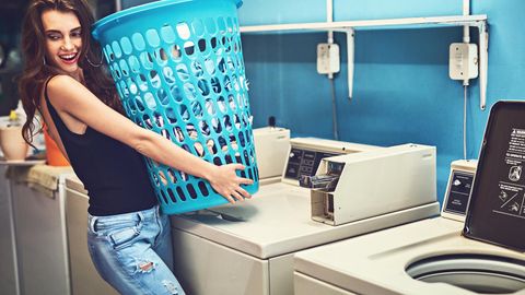 Shot of an attractive young woman holding a basket of washing while standing inside of a laundry room during the day