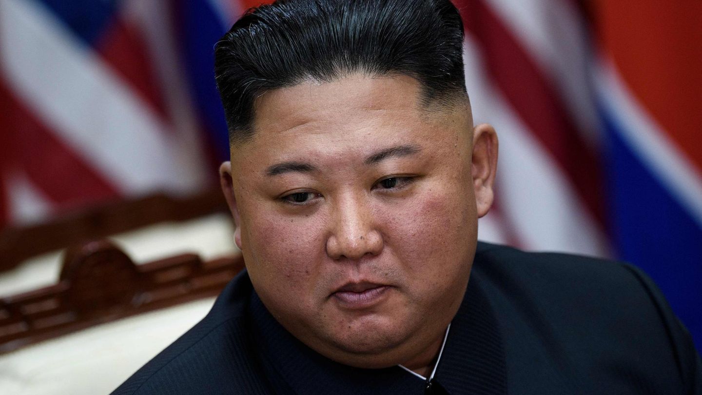Kim Jong Un, ein wohlgenährter Mann mit schwarzem Bürstenschnitt, sitzt vor einer nordkoreanischen und einer US-Flagge