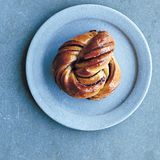 Kanel Snurre - Zimtbrötchen  Zutaten: 350 ml Vollmilch, 2 Zimtstangen oder 6 Kardamomkapseln, im Mörser grob zerstoßen, 200 g Butter, gewürfelt, 500 g Weizenmehl Type 405, 225 g Zucker, 7 g Trockenhefe, 2 EL gemahlener Zimt oder Kardamom, ½ TL Salz, 2 TL Sonnenblumenöl, zum Einölen, 1 Eigelb, mit 2 EL Milch verquirlt, zum Bepinseln 2–3 EL Hagelzucker (optional)      Zubereitung: Milch, Zimtstangen bzw. Kardamomkapseln und 50 g Butter leicht erwärmen. Mehl, 75 g Zucker, Hefe, 1 TL gemahlenen Zimt oder Kardamom und das Salz in einer Schüssel mischen. Die Zimtstangen bzw. Kardamomkapseln entfernen, die Milch langsam zur Mehlmischung geben und mit dem Knethaken einer Küchenmaschine zu einem geschmeidigen Teig verkneten. In eine geölte Schüssel geben und an einem warmen Ort gehen lassen, bis sich das Teigvolumen verdoppelt hat.  Für die Gewürz-Zucker-Mischung den übrigen gemahlenen Zimt bzw. Kardamom mit 150 g Zucker vermengen. 3 EL zurückbehalten, den Rest des Gewürzzuckers mit der übrigen Butter mischen.  Den Teig nochmals verkneten und auf einer bemehlten Arbeitsfläche zu einem 35 x 45 cm großen Rechteck ausrollen und mit der Gewürzbutter bestreichen. Von der einen Längsseite her bis zur Mitte falten, dann den Teig von der anderen Seite darüberfalten, so dass ein kleineres Rechteck entsteht. Dieses dann in zwölf 3 ½ x 11 cm breite Streifen schneiden. Jeden Streifen nochmals mittig in zwei schmalere Streifen schneiden, dabei darauf achten, dass er an einem Ende nicht durchtrennt wird. Die beiden entstandenen Streifen in die entgegengesetzte Richtung jeweils dreimal um sich selbst zwirbeln und zu einem Knoten formen. Die beiden Enden unter den Knoten stecken. Die Brötchen auf zwei mit Backpapier versehene Backbleche legen, zudecken und an einem warmen Ort gehen lassen, bis sie ihre Größe verdoppelt haben.  Den Ofen auf 190 °C (Ober-/Unterhitze) vorheizen. Die Brötchen mit dem verquirlten Ei bepinseln und nach Belieben mit dem Hagelzucker bestreuen. Im Ofen backen, bis sie leicht goldbraun geworden sind.  Den übrigen Gewürzzucker mit 50 ml Wasser erhitzen, bis er sich aufgelöst hat, dann 3 Minuten zu einem Sirup einkochen. Abkühlen lassen. Die Brötchen während des Abkühlens zwei- bis dreimal mit dem Sirup bepinseln.