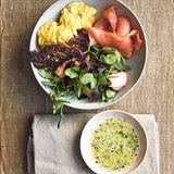 Geräucherter Lachs  Zutaten: 100 g altbackenes Roggenbrot, sehr dünn geschnitten, 50 g Parmesan, fein gerieben, 4 EL Buttermilch, 2 EL Traubenkernöl, 2 EL Apfelessig, 1 EL Schnittlauch, gehackt, 1 EL glatte Petersilie, gehackt, Salz, schwarzer Pfeffer aus der Mühle, 4 große Bio-Eier, 1 Schuss Milch, 15 g Butter, 150 g heißgeräucherter Lachs, 75 g Erbsenranken, 50 g junger roter Spinat, 50 g Wasserkresse, 150 g kaltgeräucherter Lachs      Zubereitung:  Den Ofen auf 180 °C (Ober-/Unterhitze) vorheizen. Das Brot dünn mit Öl bepinseln und mit Parmesan bestreuen. Auf ein mit Backpapier ausgelegtes Backbleich legen. 20 Minuten backen, bis es knusprig geworden ist.  In der Zwischenzeit ein Dressing aus der Buttermilch, dem Öl und dem Essig herstellen. Den Schnittlauch und die Petersilie untermischen und nach Belieben mit Salz und Pfeffer abschmecken.  Die Eier in einer Schüssel verquirlen, dann Milch und Salz zugeben und 1–2 Minuten schaumig schlagen.  Die Butter in einer Bratpfanne (Durchmesser 20 cm) erhitzen, bis sie leicht schäumt. Die Eier zugeben und 1–2 Minuten stocken lassen, dann mit einem Spatel von den Seiten aus in die Mitte schieben, so dass die noch flüssige Eimasse seitlich zu den Rändern herausläuft. Diesen Vorgang wiederholen, bis die Eier gestockt, aber noch nicht ganz fest sind.  Den heißgeräucherten Lachs vorsichtig mit einer Gabel in eine Schüssel zerteilen. 2–3 EL des Dressings und die Salatblätter dazugeben und alles vorsichtig schwenken.  Zum Anrichten den Salat mit dem heißgeräucherten Lachs auf zwei Schalen aufteilen, dann den kaltgeräucherten Lachs und dann das Rührei dazugeben. Zum Schluss die Roggencroutons obenauf legen und mit dem übrigen Dressing servieren.