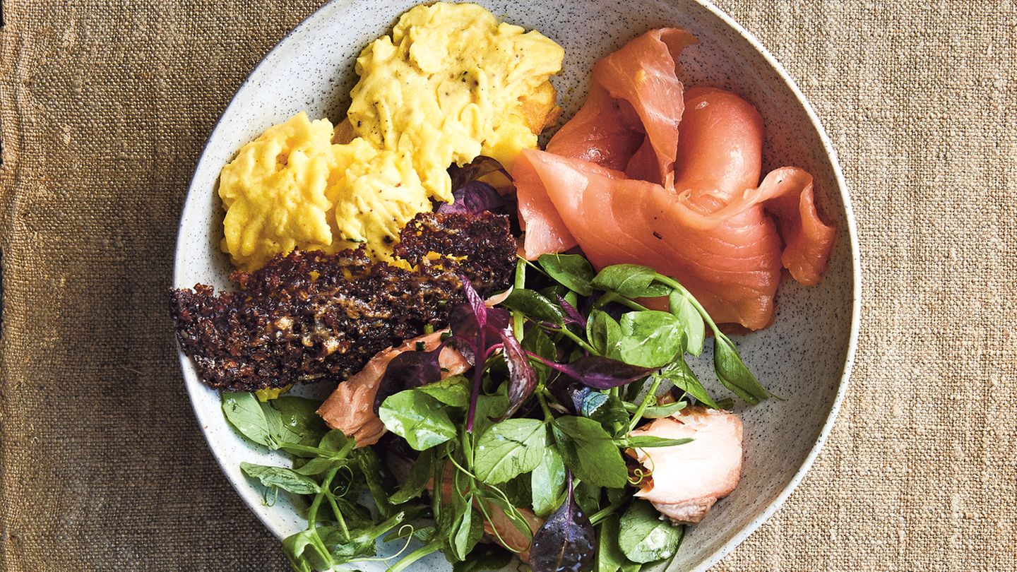 Geräucherter Lachs  Zutaten: 100 g altbackenes Roggenbrot, sehr dünn geschnitten, 50 g Parmesan, fein gerieben, 4 EL Buttermilch, 2 EL Traubenkernöl, 2 EL Apfelessig, 1 EL Schnittlauch, gehackt, 1 EL glatte Petersilie, gehackt, Salz, schwarzer Pfeffer aus der Mühle, 4 große Bio-Eier, 1 Schuss Milch, 15 g Butter, 150 g heißgeräucherter Lachs, 75 g Erbsenranken, 50 g junger roter Spinat, 50 g Wasserkresse, 150 g kaltgeräucherter Lachs      Zubereitung:  Den Ofen auf 180 °C (Ober-/Unterhitze) vorheizen. Das Brot dünn mit Öl bepinseln und mit Parmesan bestreuen. Auf ein mit Backpapier ausgelegtes Backbleich legen. 20 Minuten backen, bis es knusprig geworden ist.  In der Zwischenzeit ein Dressing aus der Buttermilch, dem Öl und dem Essig herstellen. Den Schnittlauch und die Petersilie untermischen und nach Belieben mit Salz und Pfeffer abschmecken.  Die Eier in einer Schüssel verquirlen, dann Milch und Salz zugeben und 1–2 Minuten schaumig schlagen.  Die Butter in einer Bratpfanne (Durchmesser 20 cm) erhitzen, bis sie leicht schäumt. Die Eier zugeben und 1–2 Minuten stocken lassen, dann mit einem Spatel von den Seiten aus in die Mitte schieben, so dass die noch flüssige Eimasse seitlich zu den Rändern herausläuft. Diesen Vorgang wiederholen, bis die Eier gestockt, aber noch nicht ganz fest sind.  Den heißgeräucherten Lachs vorsichtig mit einer Gabel in eine Schüssel zerteilen. 2–3 EL des Dressings und die Salatblätter dazugeben und alles vorsichtig schwenken.  Zum Anrichten den Salat mit dem heißgeräucherten Lachs auf zwei Schalen aufteilen, dann den kaltgeräucherten Lachs und dann das Rührei dazugeben. Zum Schluss die Roggencroutons obenauf legen und mit dem übrigen Dressing servieren.