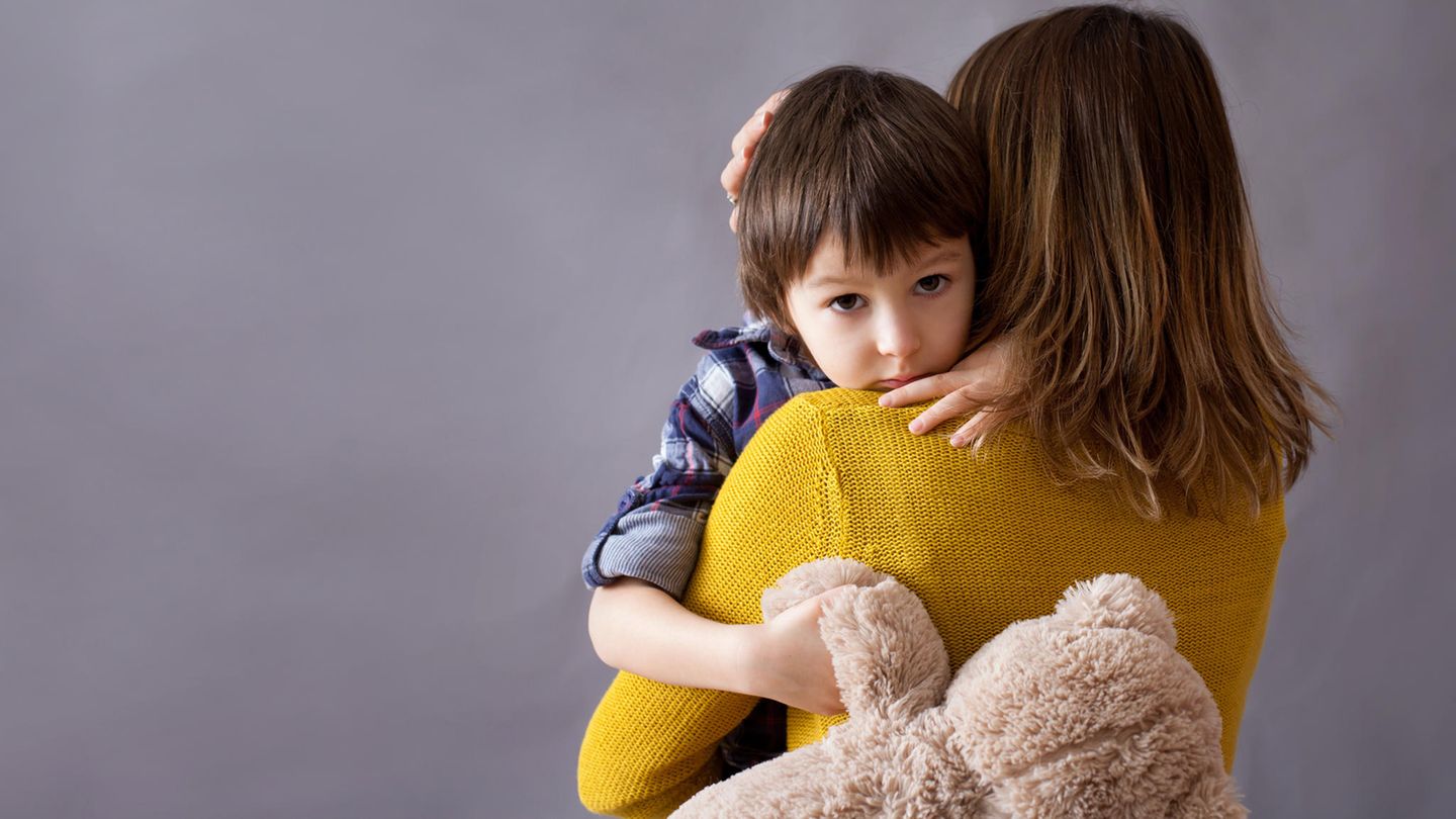 Eine Frau umarmt einen Jungen, der einen Teddybär hält