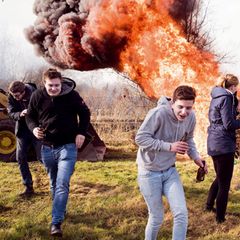 Jugendliche rennen vor einem großen Feuer davon