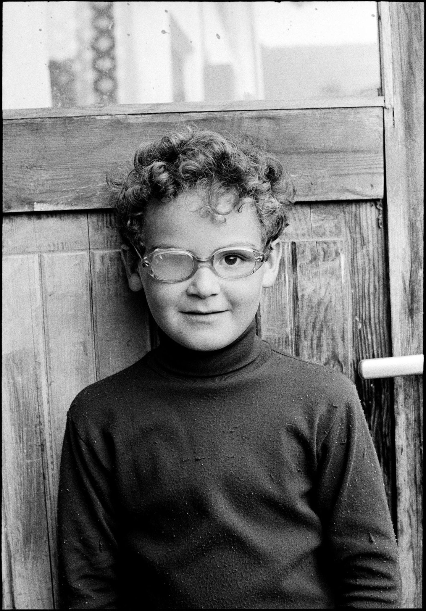 Ein kleiner lockiger Junge mit einer Brille, mit einem blinden Glas