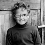 Ein kleiner lockiger Junge mit einer Brille, mit einem blinden Glas