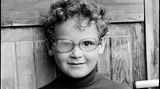 Ein kleiner lockiger Junge mit einer Brille, mit einem blinden Glas