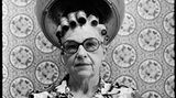 Eine alte Frau mit Brille sitzt unter einer Trockenhaube